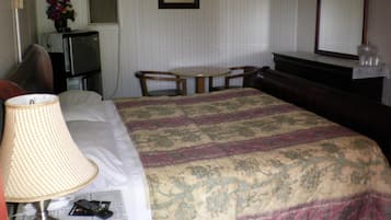 Une chambre d’hôtel comprenant un lit, une table de chevet avec une lampe, une petite table avec des chaises, une commode, un miroir et un radiateur fixé au mur.