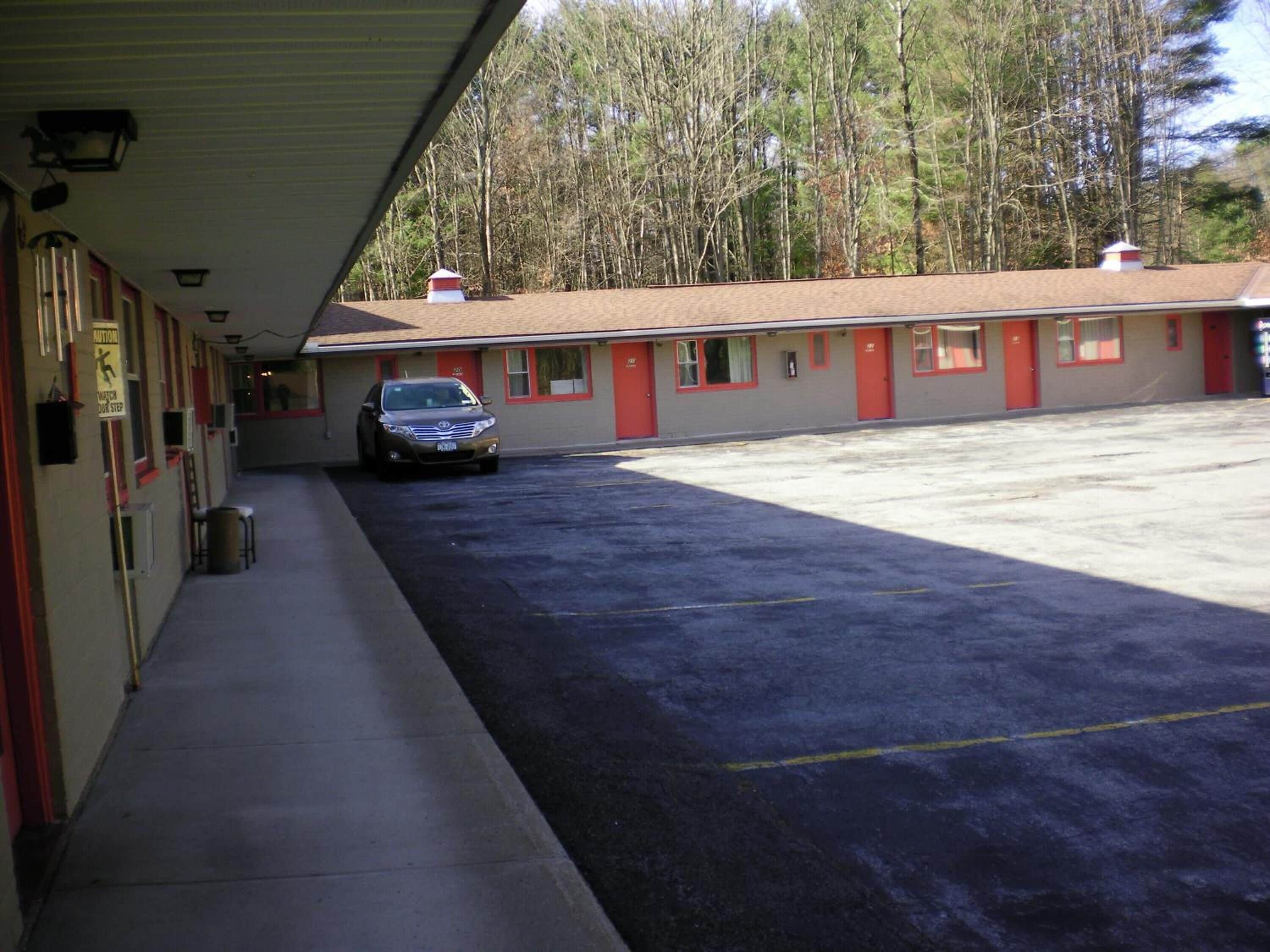A motel with a covered parking area and a row of rooms with red trim.
