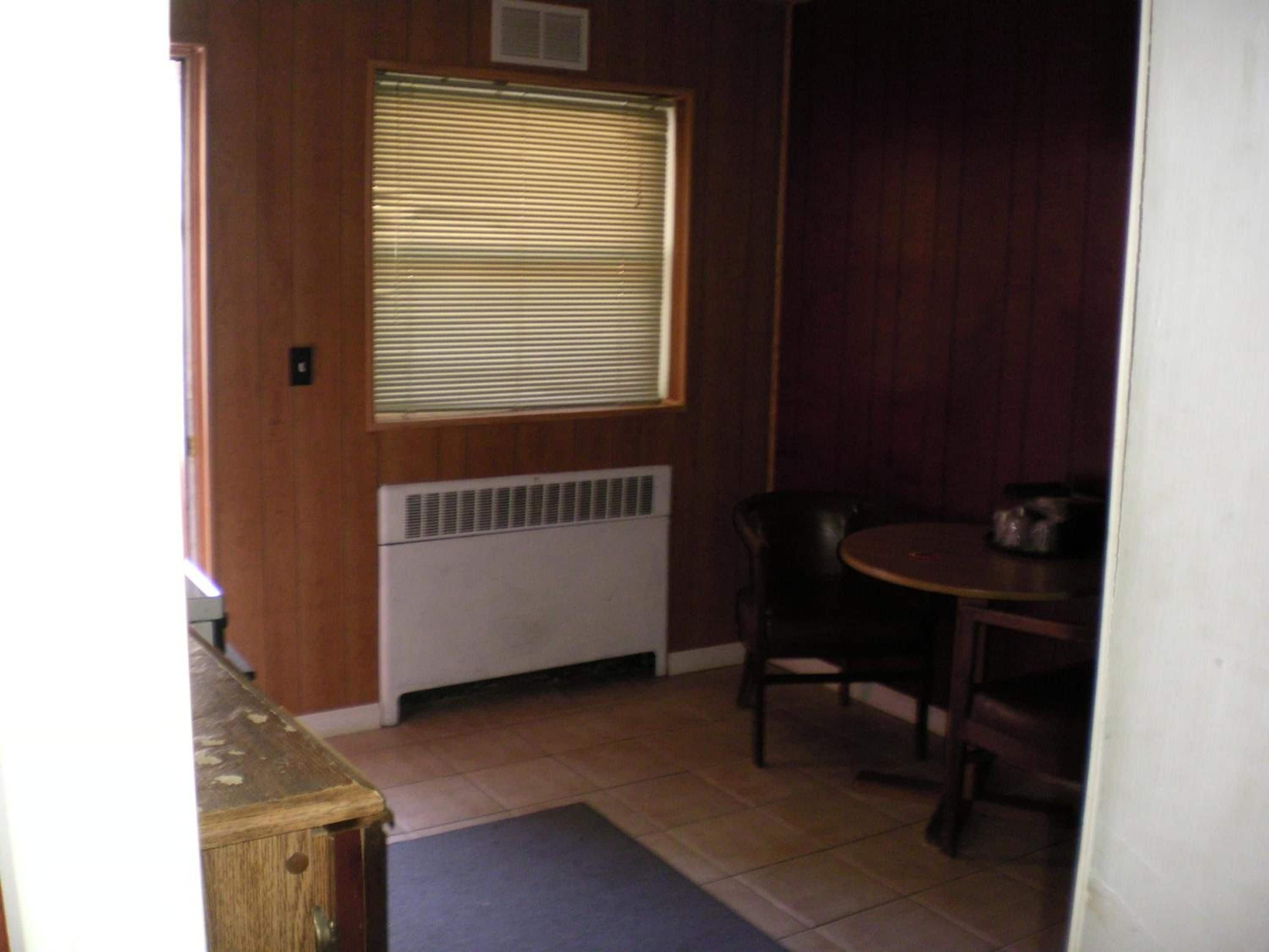 Une pièce avec un radiateur, une fenêtre équipée de stores, une table à manger avec des chaises et un meuble en bois.