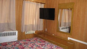 A bedroom with wooden walls, a bed with a floral bedspread, a television mounted on the wall, and a window with curtains. - The Rome Motel (Rome)