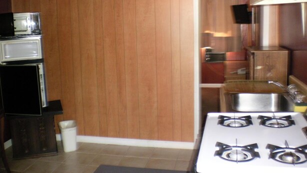 A kitchen with wooden paneling, a stove, a microwave, and a trash bin. - The Rome Motel (Rome)