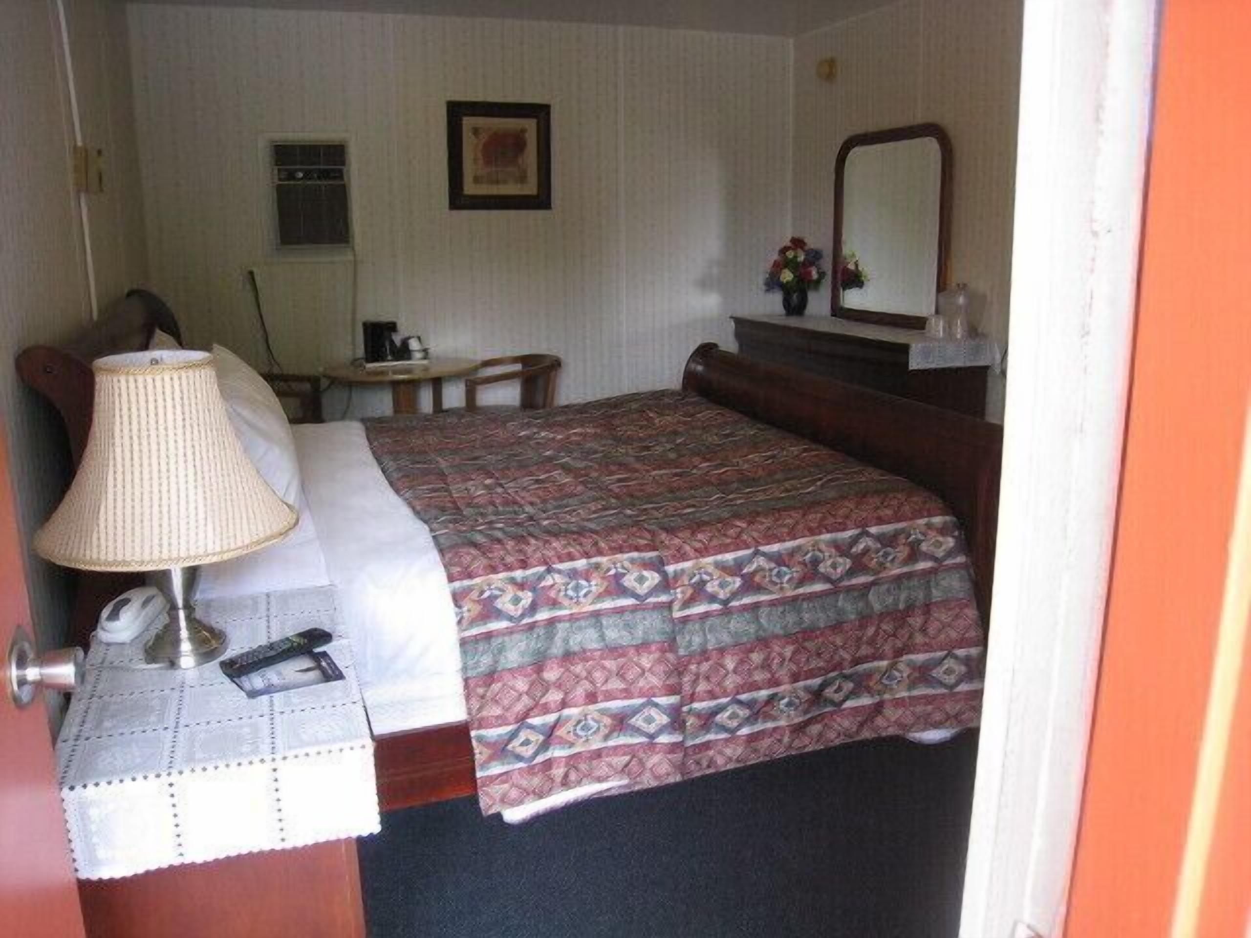 A hotel room with a bed, a desk with a lamp, a chair, a dresser, and a mirror.