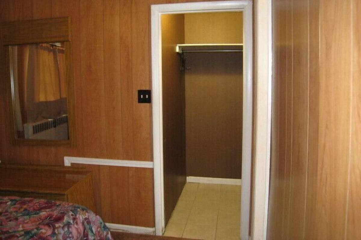 A room with wooden paneling, a bed with a floral bedspread, a mirror, and a closet with a hanging rod.
