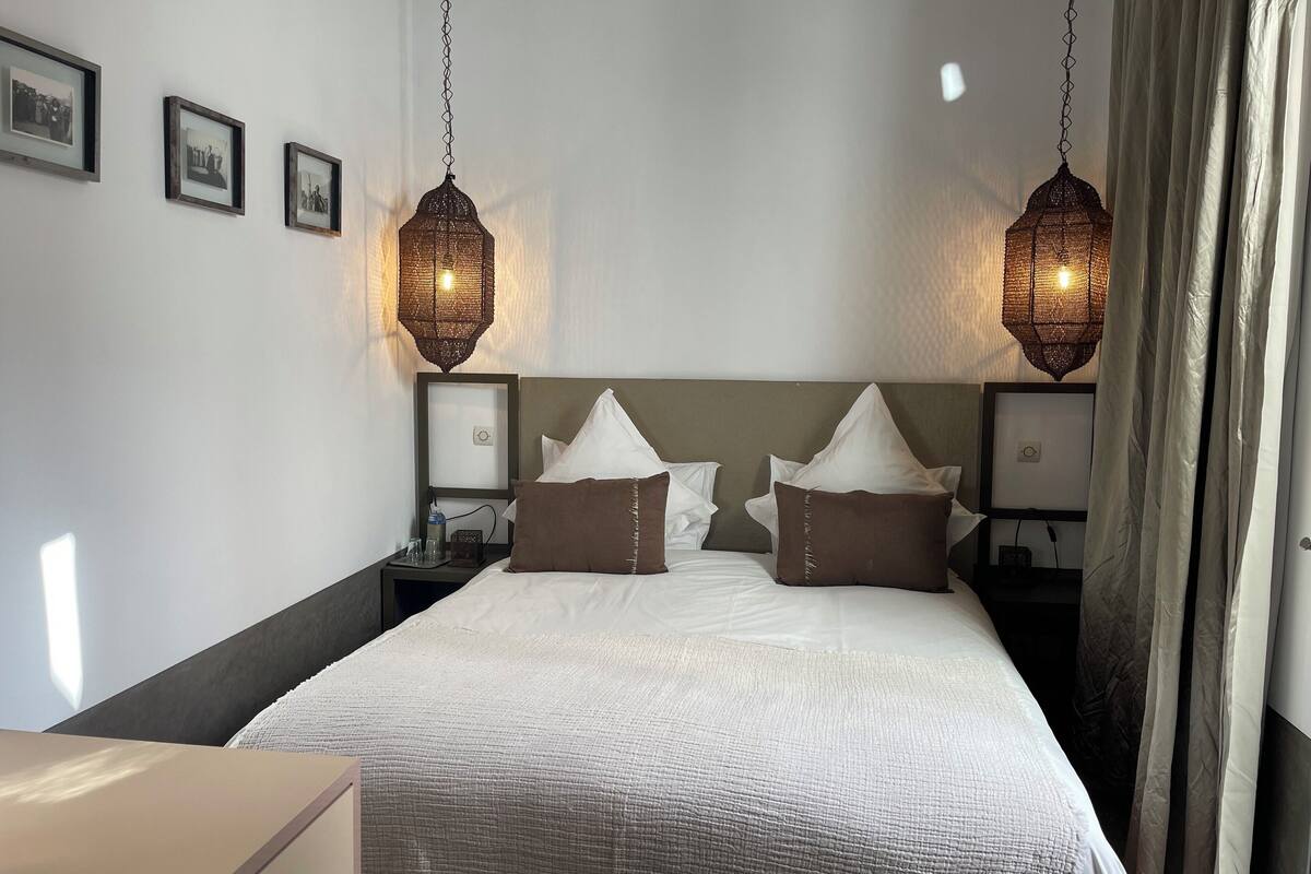A neatly made bed with white linens and brown pillows, two bedside tables with lamps, and framed pictures on the wall.