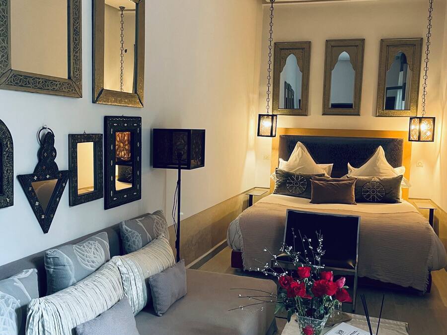 A bedroom with a large bed, a sofa, and multiple wall-mounted mirrors.
