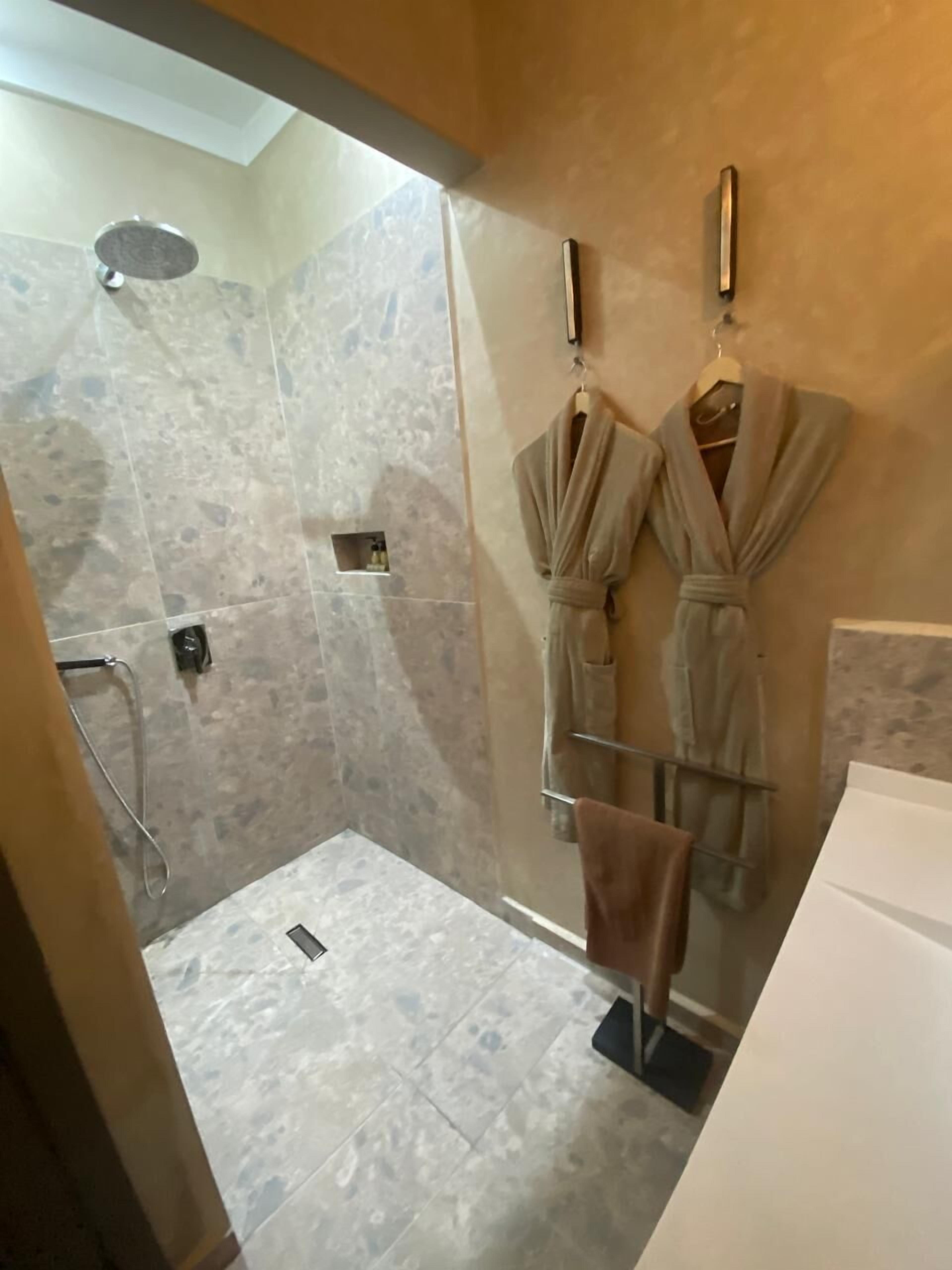 A modern bathroom with a shower, marble tiles, and two robes hanging on hooks.