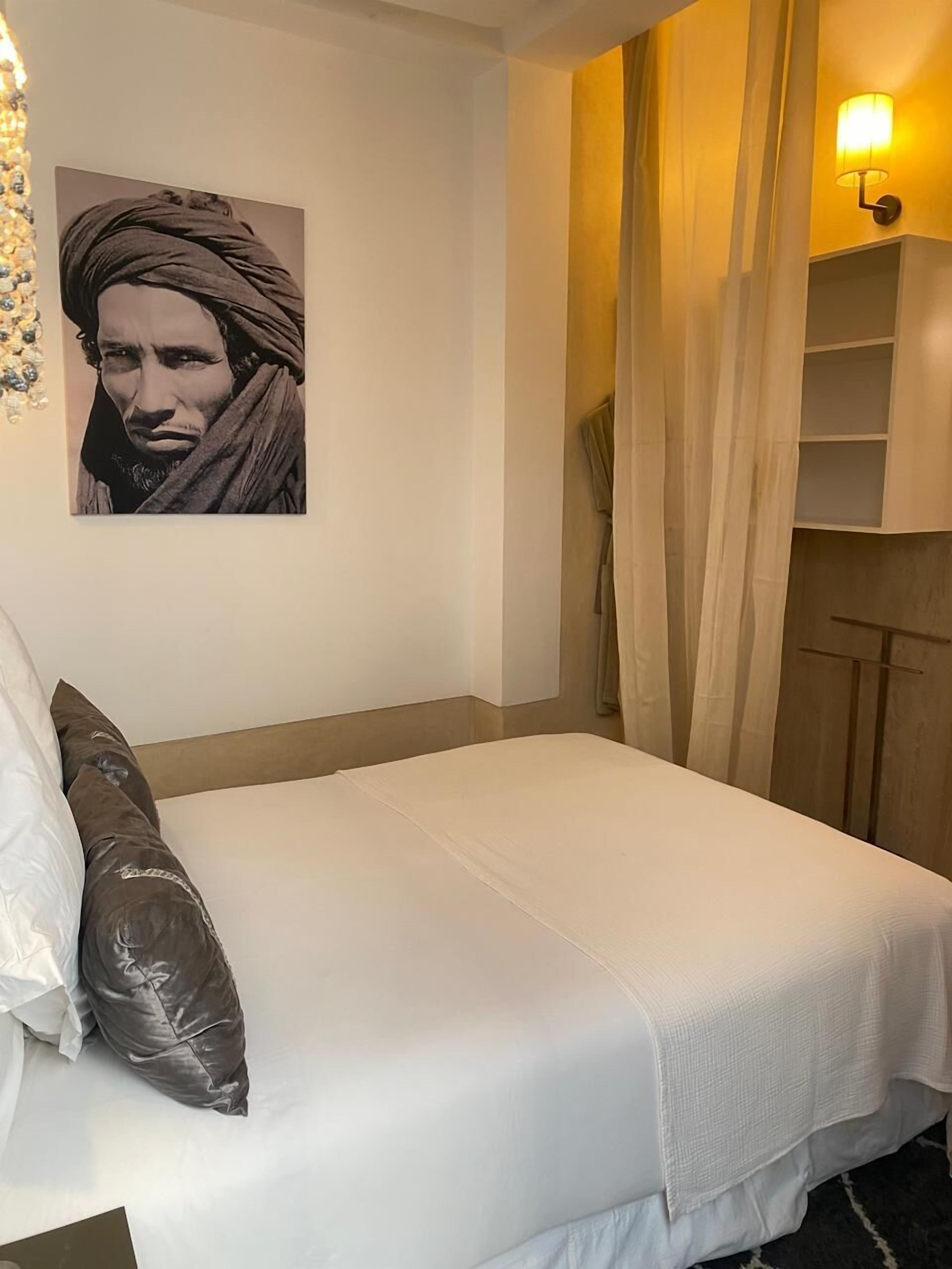 Een hotelkamer met een bed, een kunstwerk aan de muur, een plank met een lamp en een gordijn.