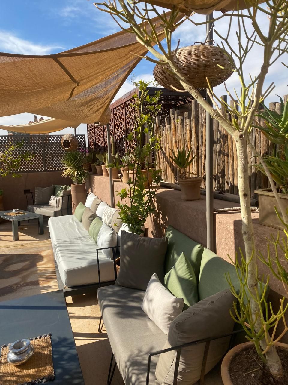 A sunlit outdoor seating area with a sofa, cushions, and potted plants.