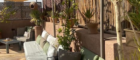 A sunlit outdoor seating area with a sofa, cushions, and potted plants.