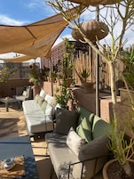 A sunlit outdoor seating area with a sofa, cushions, and potted plants.