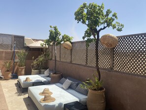 A sunlit outdoor seating area with cushioned benches and potted plants.
