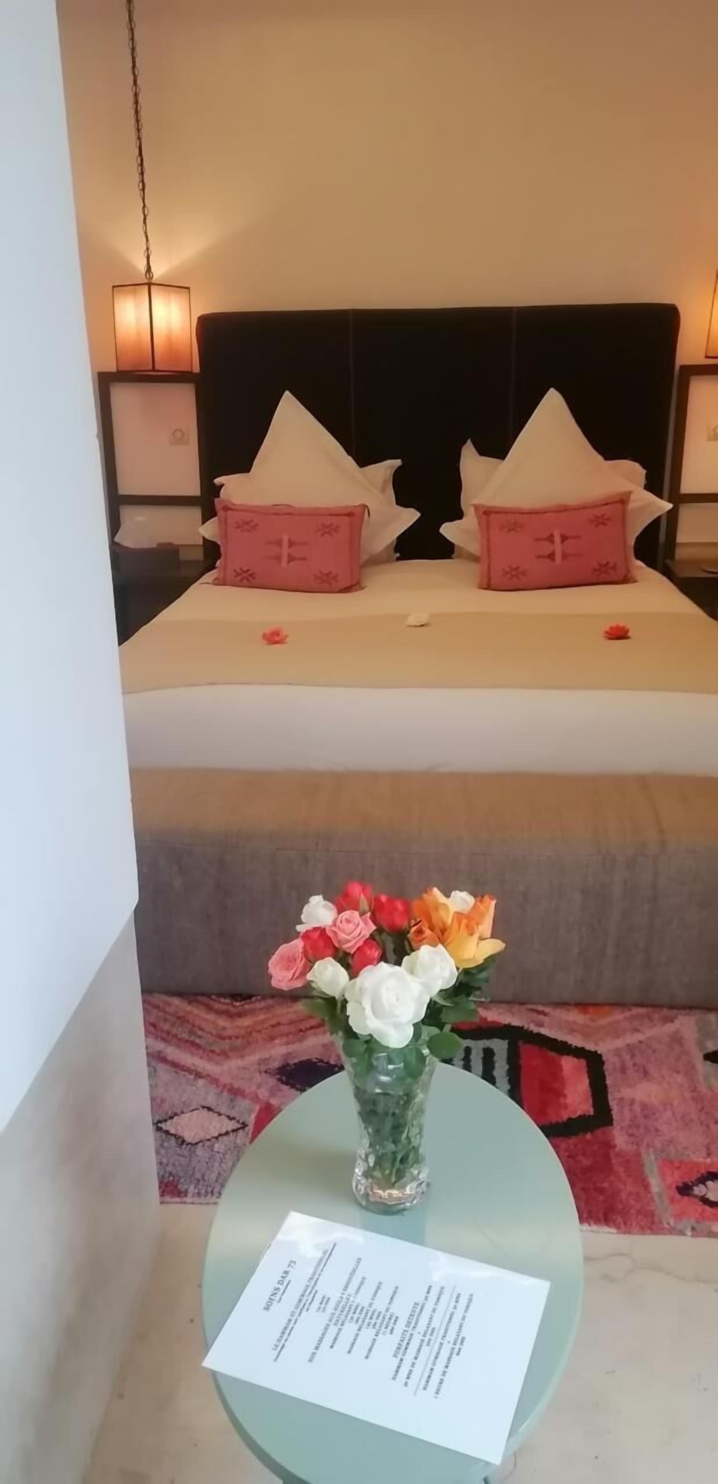 A hotel room with a bed, pillows, a vase of flowers, and a table with a document.
