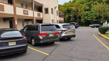 A parking lot with several cars, a building with multiple floors, and a green tree line in the background.