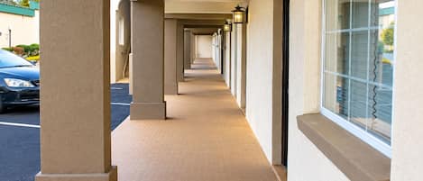 A corridor with a series of columns and windows, leading to a parking area.