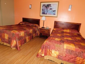 Una habitación de hotel con dos camas, una mesita de noche con lámpara y un cuadro en la pared.
