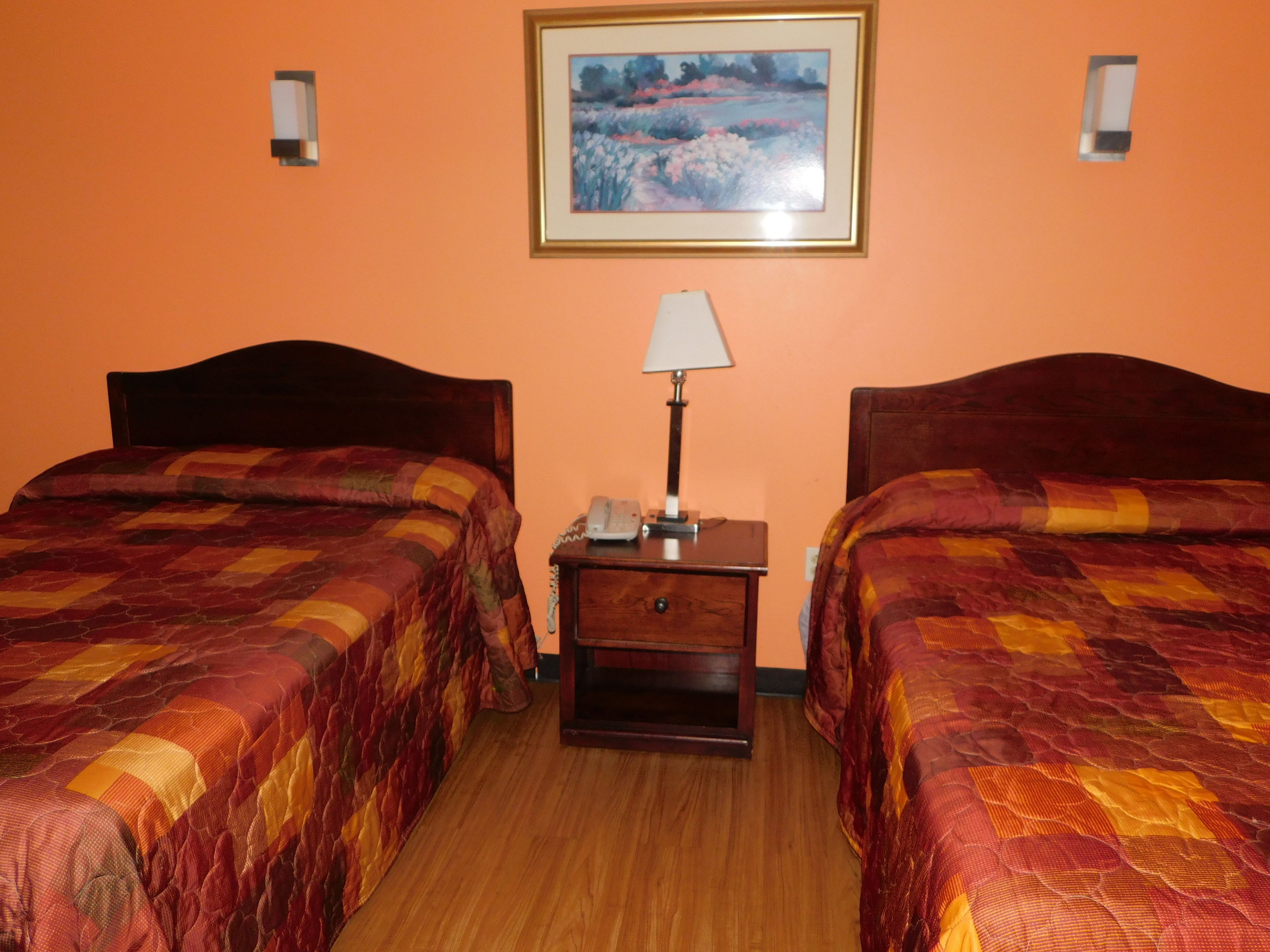 A hotel room with two beds, a nightstand with a lamp, and a framed painting on the wall.