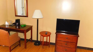 Une chambre d’hôtel avec un bureau en bois, une chaise, un téléviseur posé sur un meuble en bois, une lampe et un miroir au mur.
