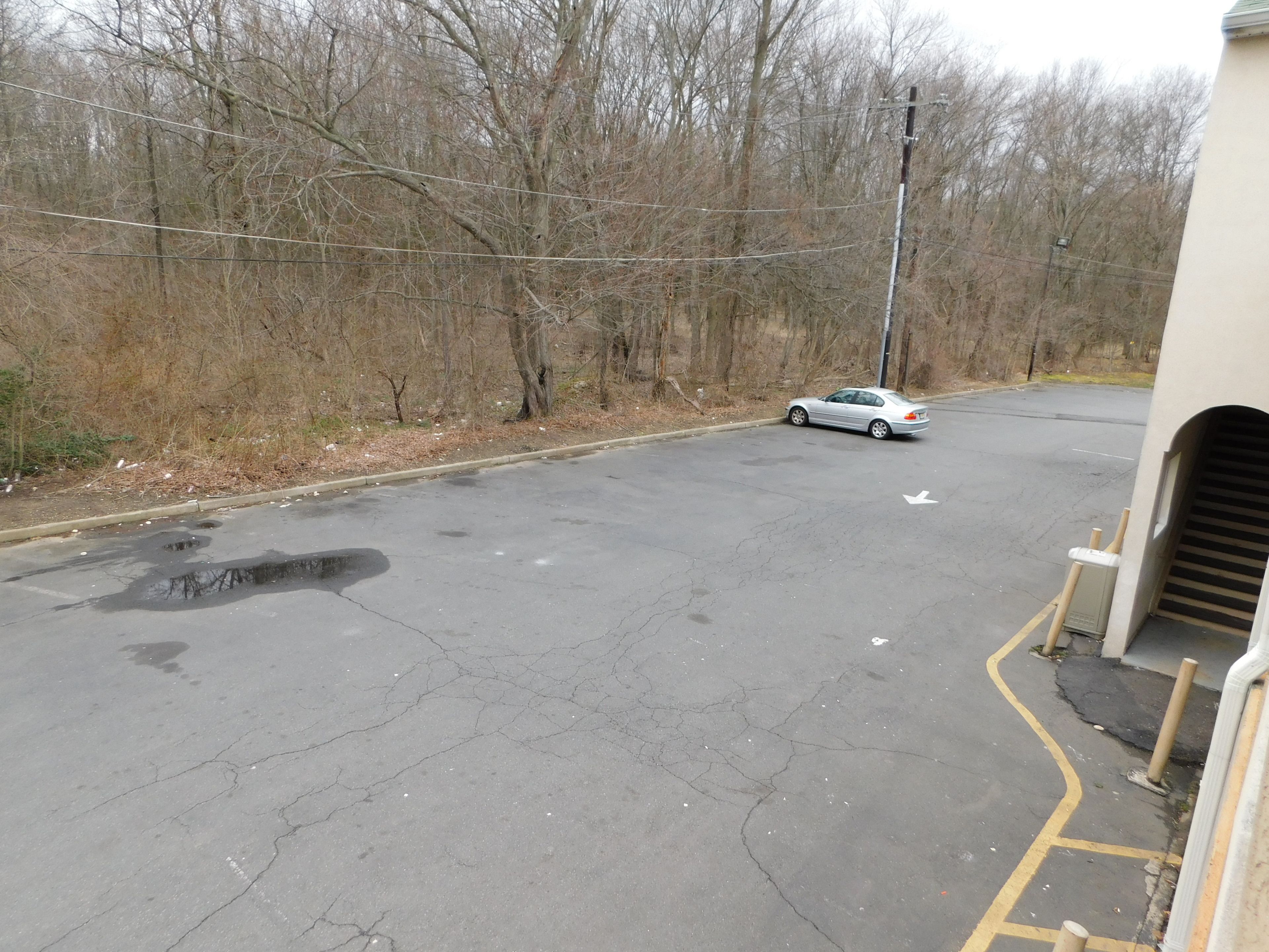 A parking area with a white car, trees, and a building with a garage entrance.