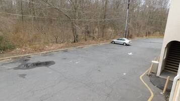 A parking area with a white car, trees, and a building with a garage entrance.