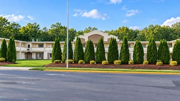 A multi-story hotel with a symmetrical facade, a central entrance, and a well-maintained lawn with trimmed hedges.