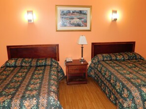 Habitación de hotel con dos camas, una mesita de noche, una lámpara y un cuadro en la pared.
