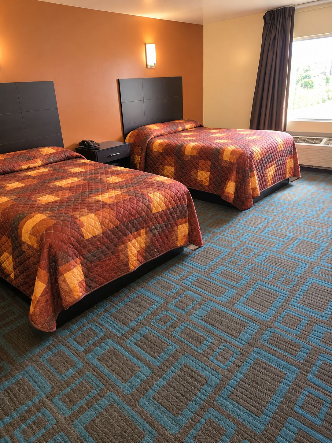 A hotel room with two beds, a nightstand, a wall-mounted lamp, and a window with curtains.