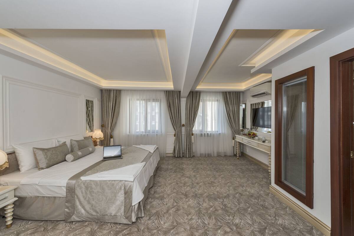 A hotel room with a large bed, a desk, a TV, and a large window with curtains.
