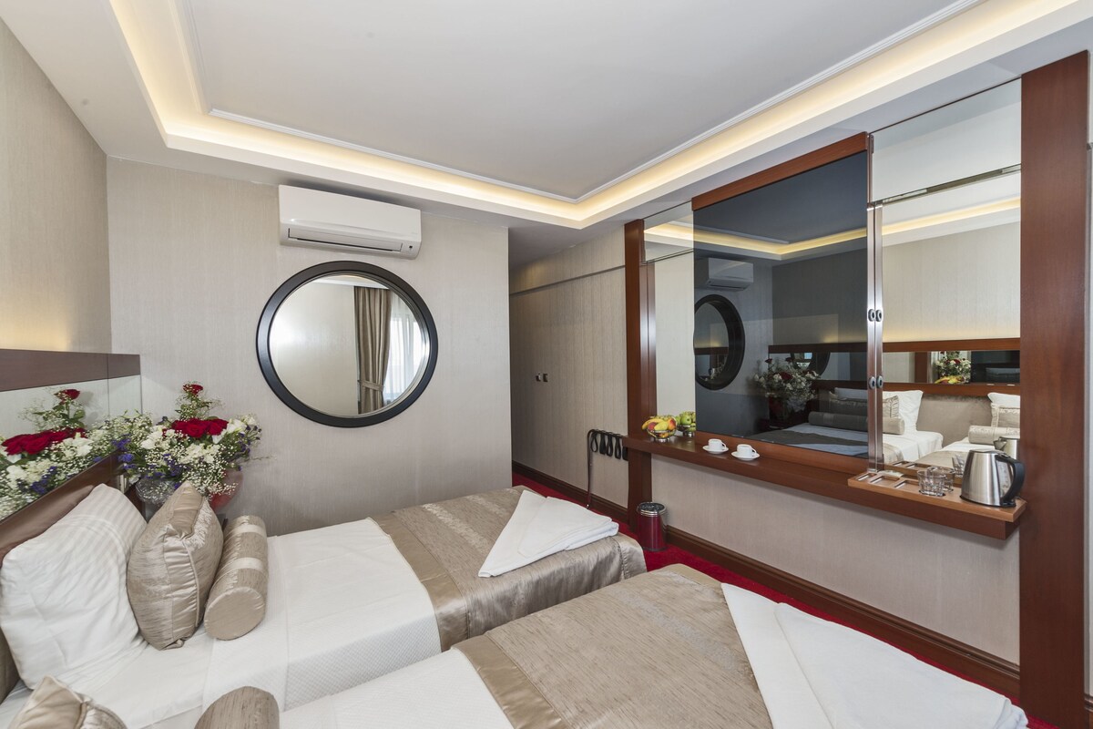 Een hotelkamer met twee bedden, een grote spiegel, een airconditioning en een klein tafeltje met waterkoker en kopjes.
