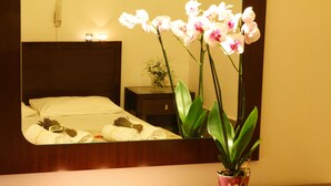 A hotel room with a bed, a nightstand with a vase of flowers, and a mirror reflecting the room. - Hotel Kostis (Skiathos)