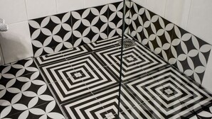 Un baño con baldosas de diseño blanco y negro, un cabezal de ducha y un desagüe.