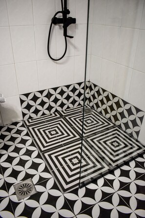 A bathroom with black and white patterned tiles, a shower head, and a drain. - Hotel Kostis (Skiathos)