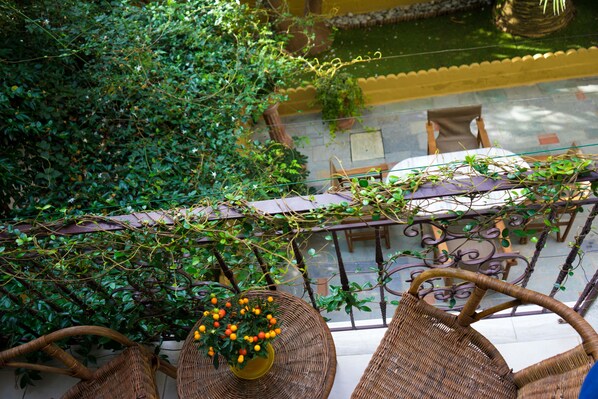 A balcony with wicker furniture, a potted plant with yellow flowers, and a view of a pool and garden area. - Hotel Kostis (Skiathos)