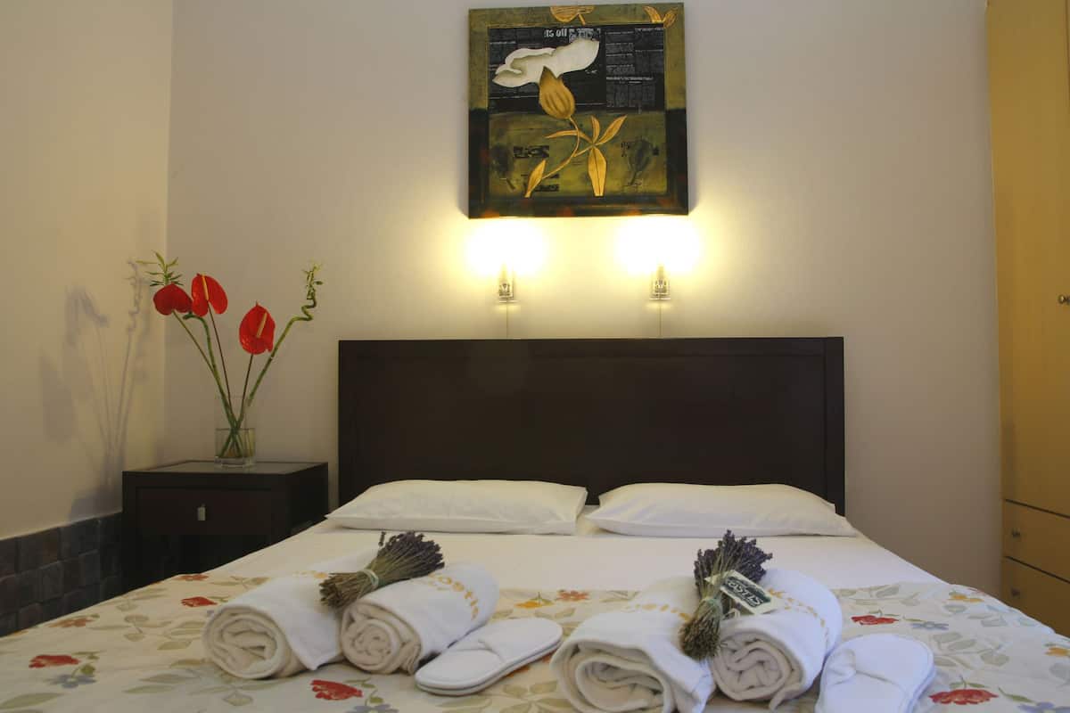 Habitación de hotel con una cama, dos lámparas de noche, una mesita de noche con un florero de flores rojas y un cuadro en la pared.