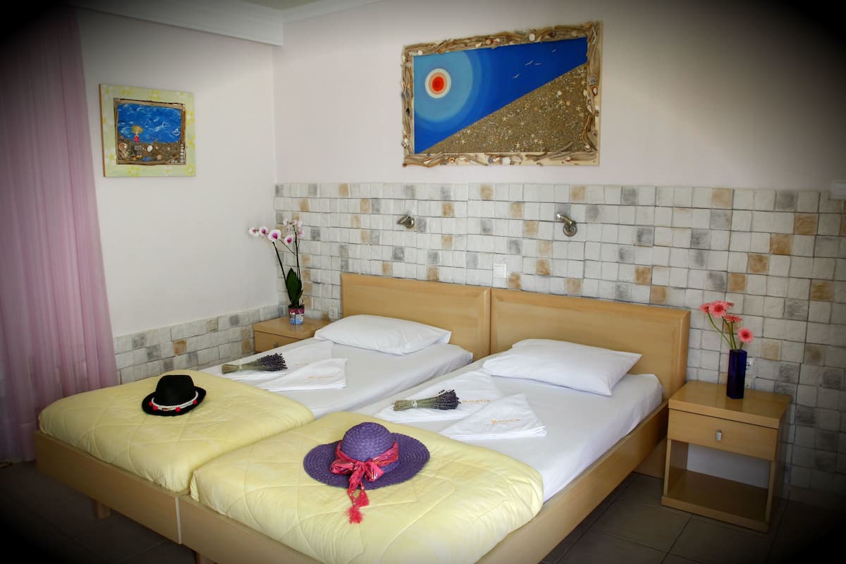 Cama doble con dos almohadas, mesita de noche con un florero y un cuadro en la pared.