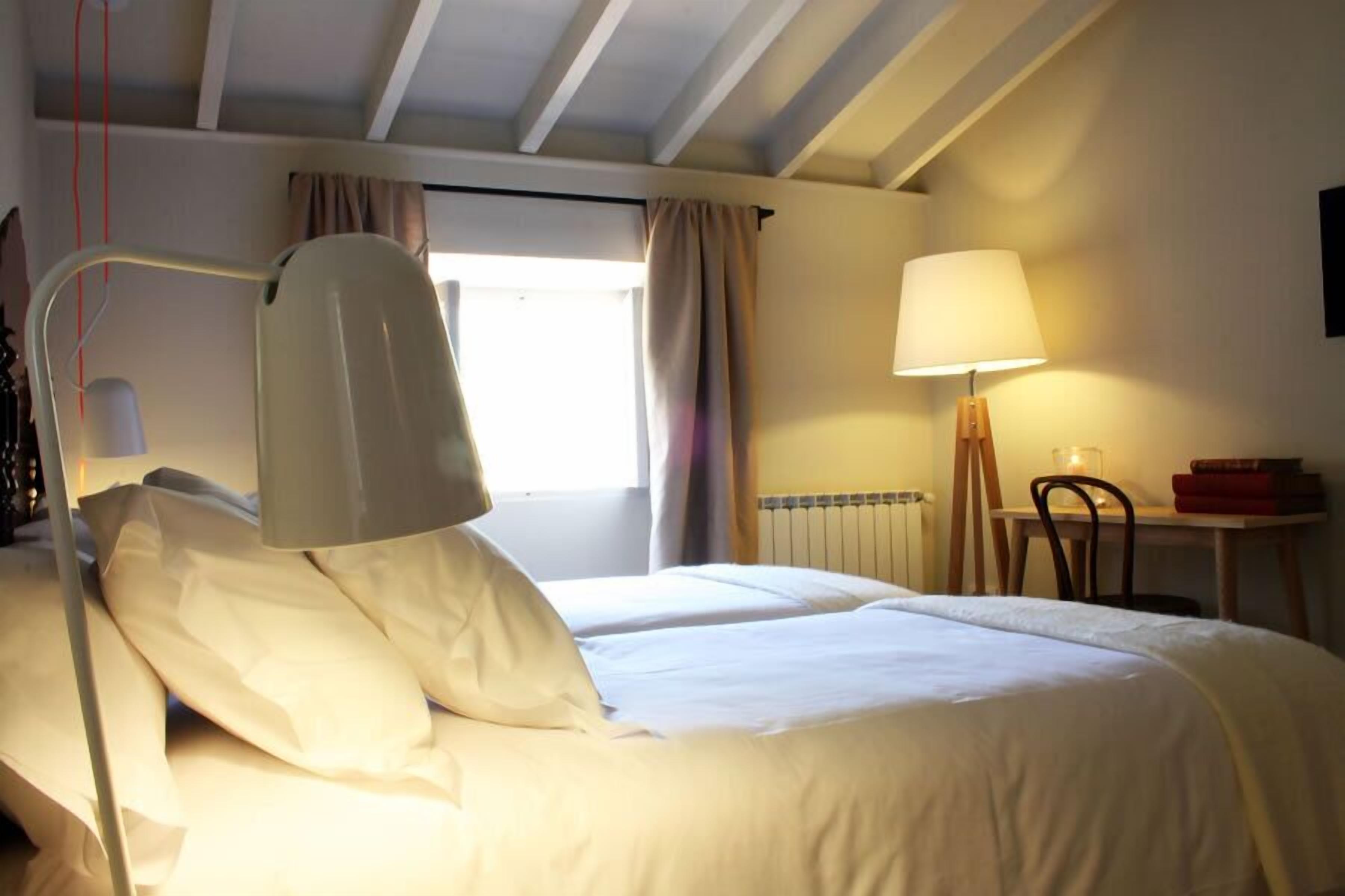 A hotel room with a bed, a desk, a lamp, and a window with curtains.