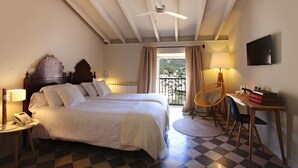 Un dormitorio con cama, mesitas de noche, una silla, escritorio, televisión y balcón con cortinas.