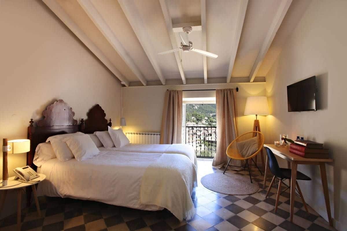 A bedroom with a bed, bedside tables, a chair, a desk, a TV, and a balcony with curtains.