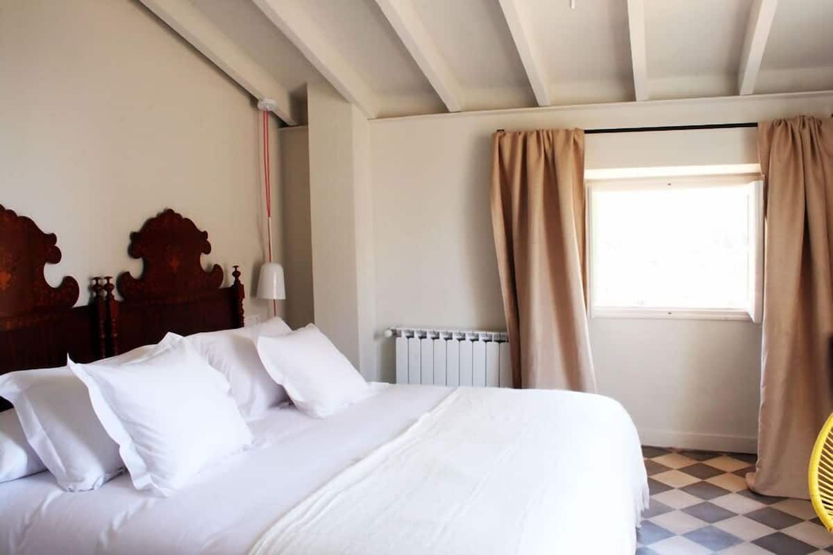 A bedroom with a large bed, a radiator, a window with curtains, and a checkered floor.