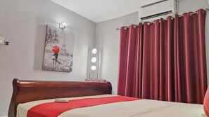Une chambre d’hôtel avec un lit, un rideau rouge, une lampe fixée au mur et un tableau représentant la Tour Eiffel.