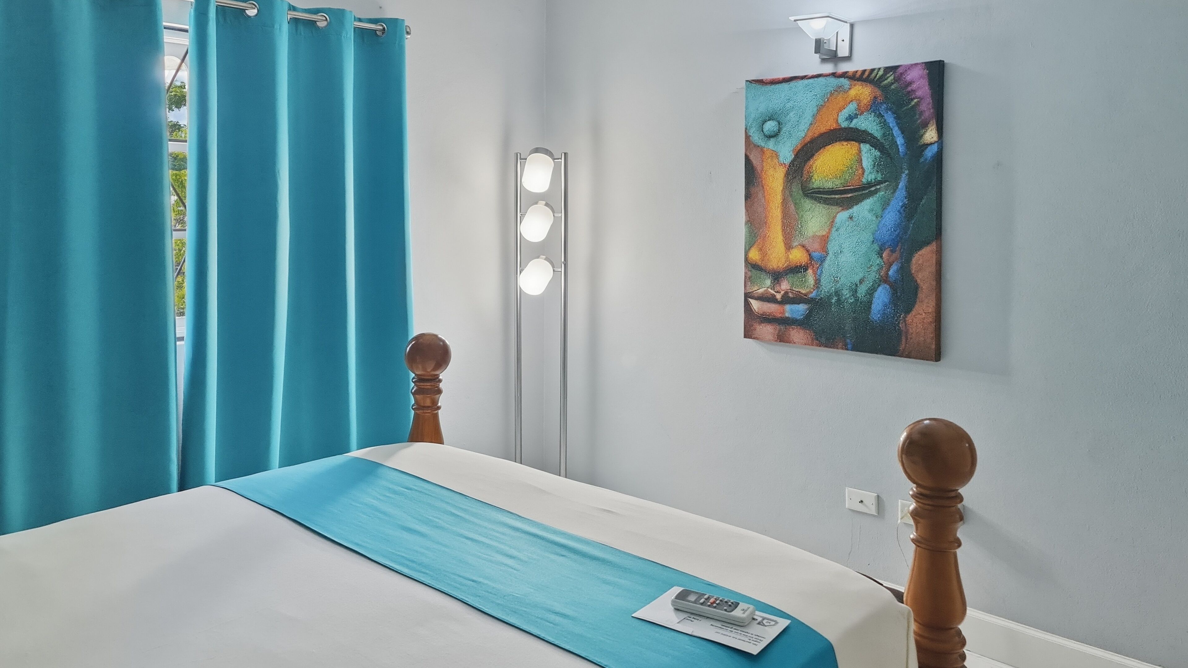 Una camera d'albergo con un letto, tende, una lampada a parete e un quadro.