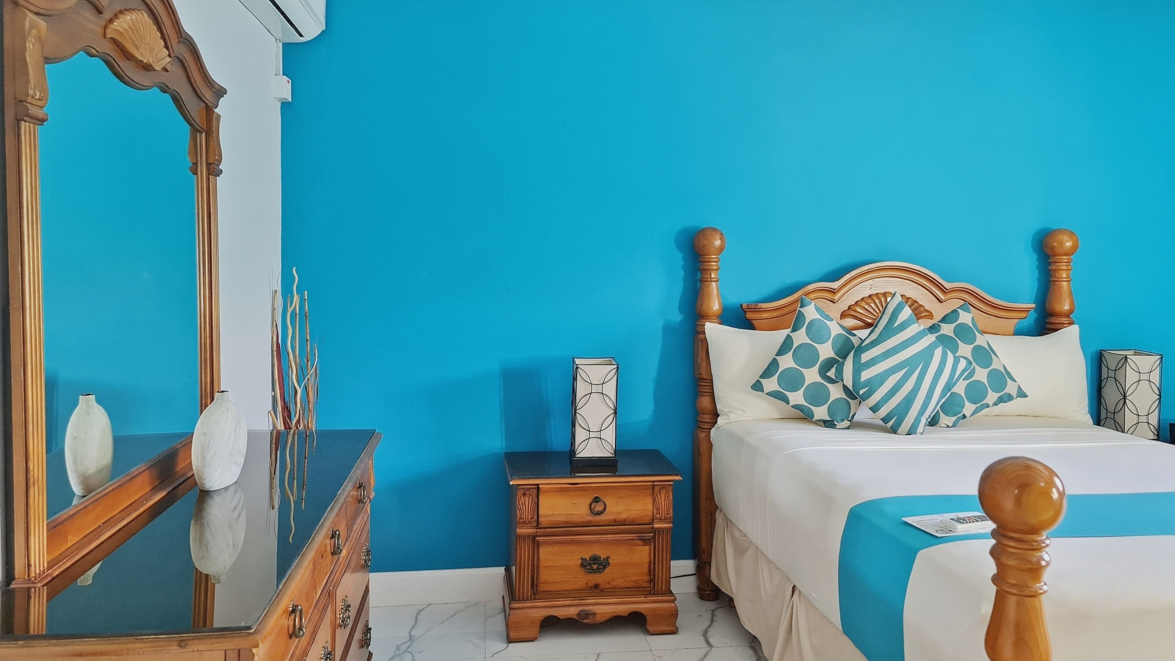 Une chambre à coucher avec un lit, une table de chevet, une commode, un miroir et un mur bleu.