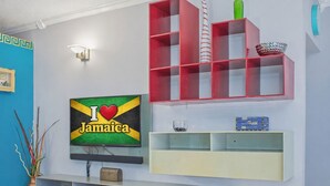 Ein Zimmer mit einem Flachbildfernseher, der 'I ♥ Jamaica' zeigt, einer rot-weiß gestreiften Vase und einem blau gemusterten Kissen.