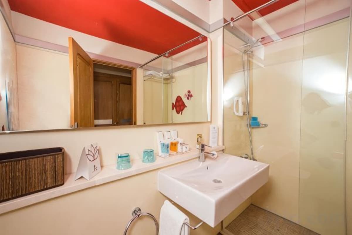 Un baño con un lavamanos blanco, un espejo, una ducha y un perchero para toallas.
