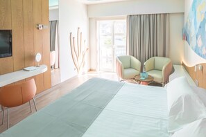 Een hotelkamer met een bed, twee fauteuils, een tafeltje, een televisie en een raam met gordijnen.