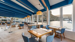 A modern restaurant with large windows, wooden tables, and blue chairs. - Hotel LIVVO Puerto de Mogán (Mogan)