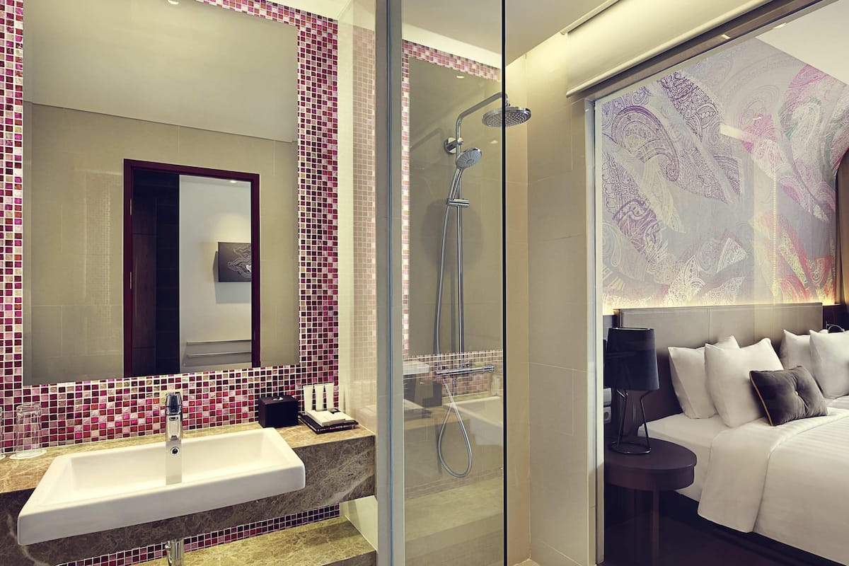 A modern bathroom with a glass shower enclosure, a large mirror, and a bed with a headboard.