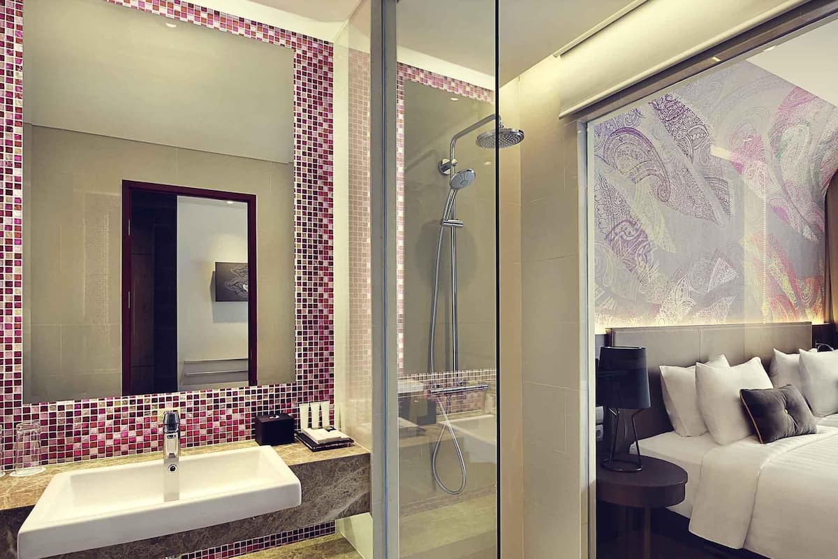 Une salle de bain moderne avec une douche en verre, un grand miroir et un lit doté d’une tête de lit.