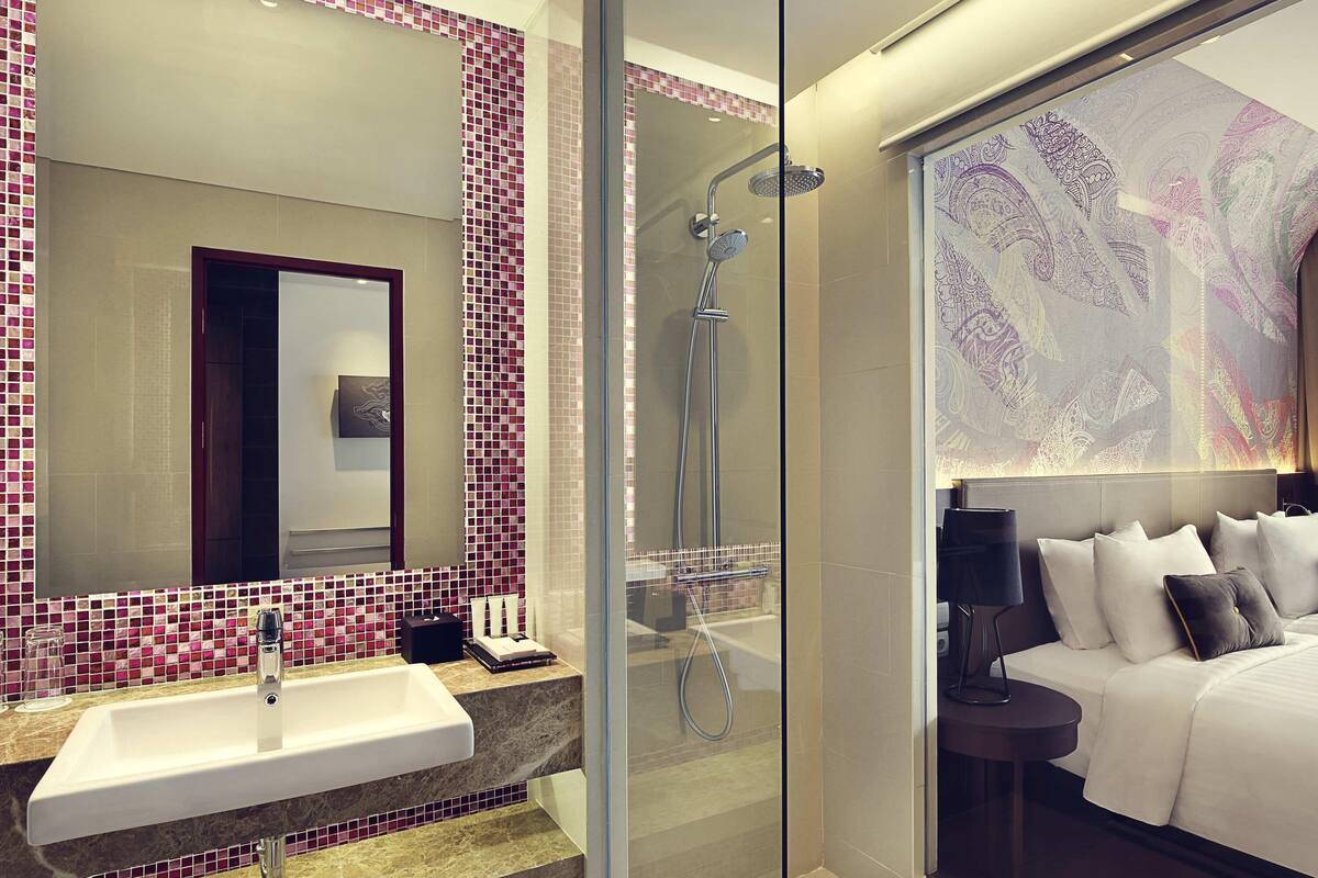 A modern bathroom with a glass shower enclosure, a large mirror, and a bed with a headboard.