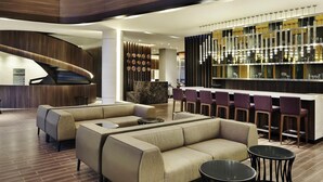 Eine moderne Lobby mit einer gebogenen Rezeption, einer Bar mit violetten Barhocker und einer Lounge mit Sofas und runden Tischen.