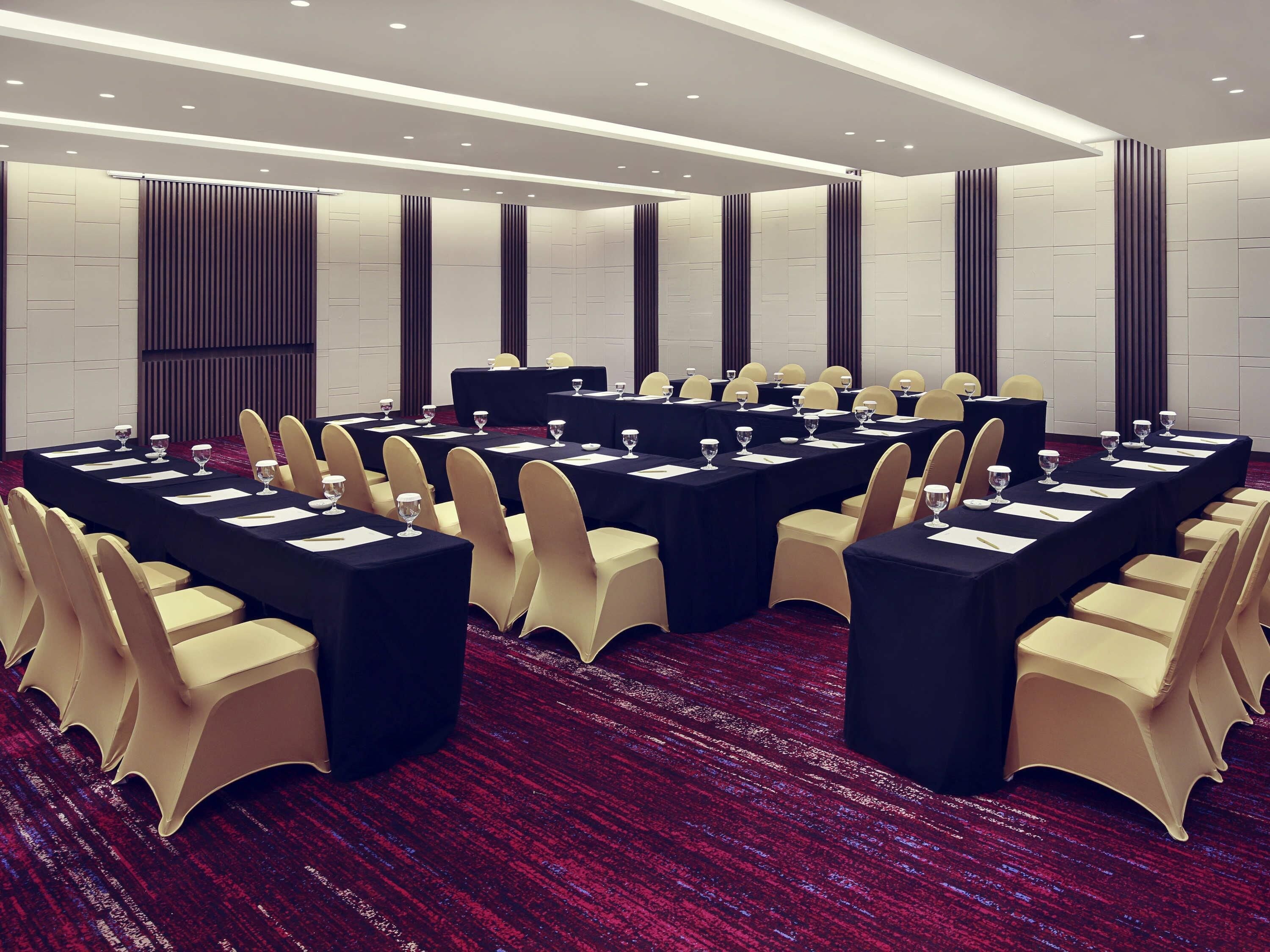 Un salón de conferencias con varias mesas, sillas y piso cubierto de alfombra roja.